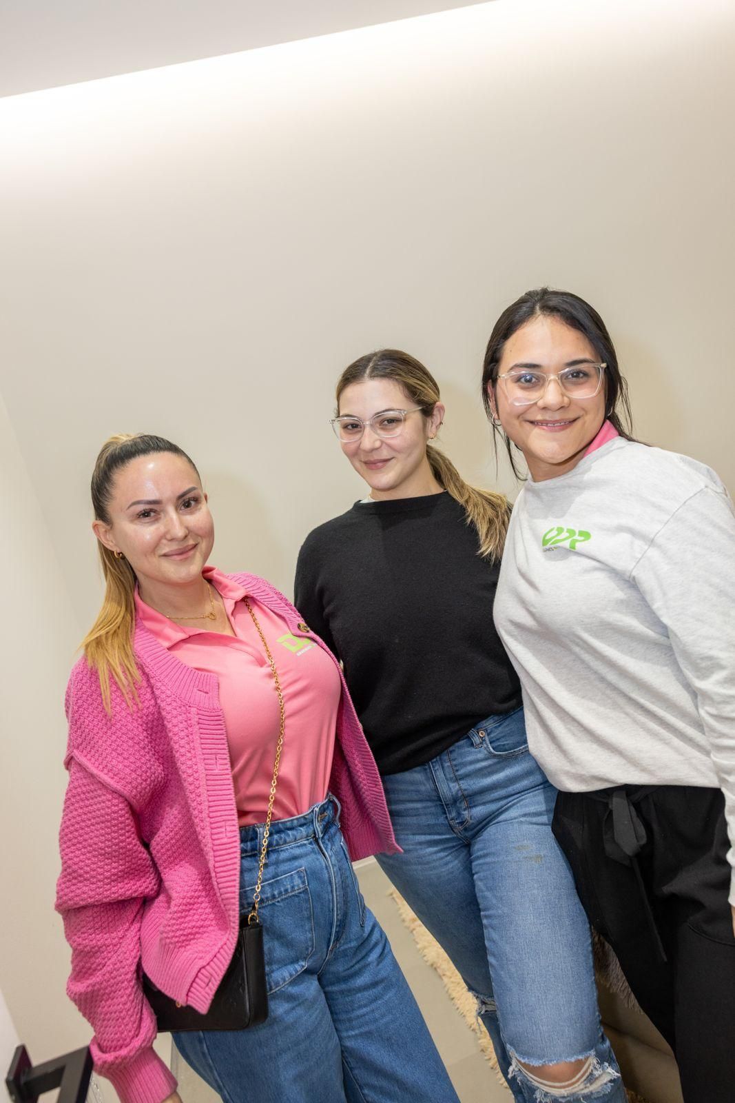 Three people standing together against a plain wall, smiling and posing for a photo.