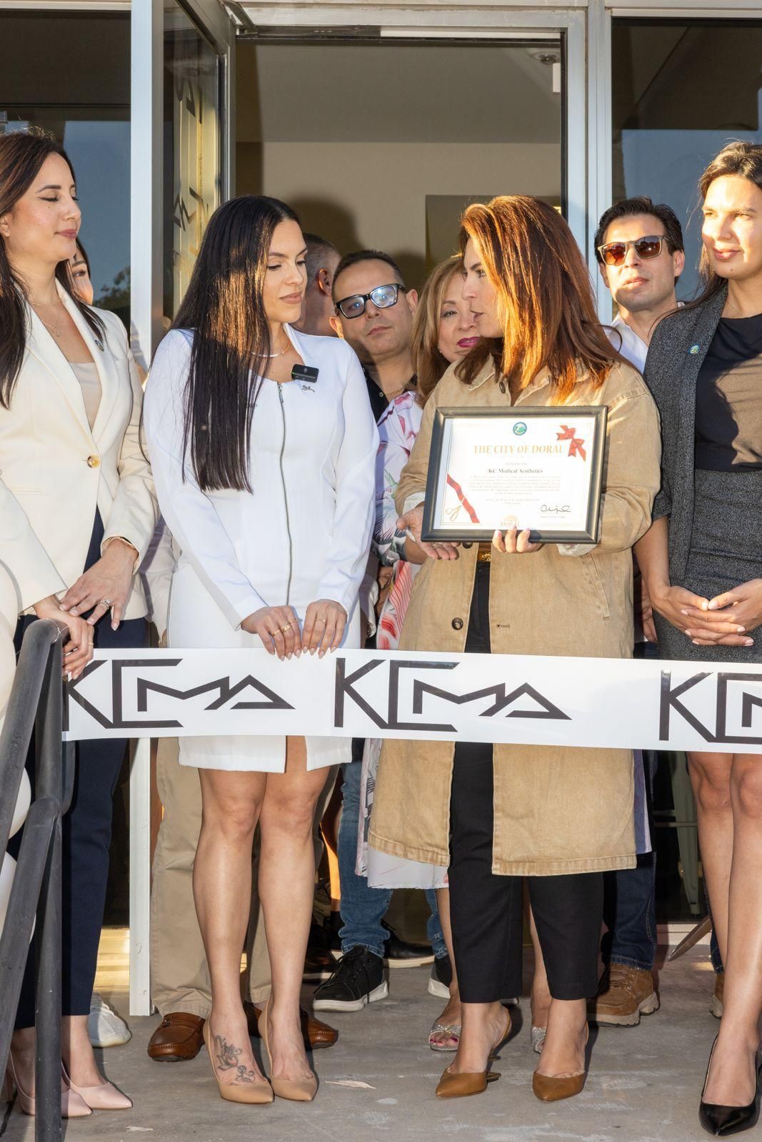 Five people participate in a ribbon-cutting ceremony, with one individual holding a framed certificate at an entrance.