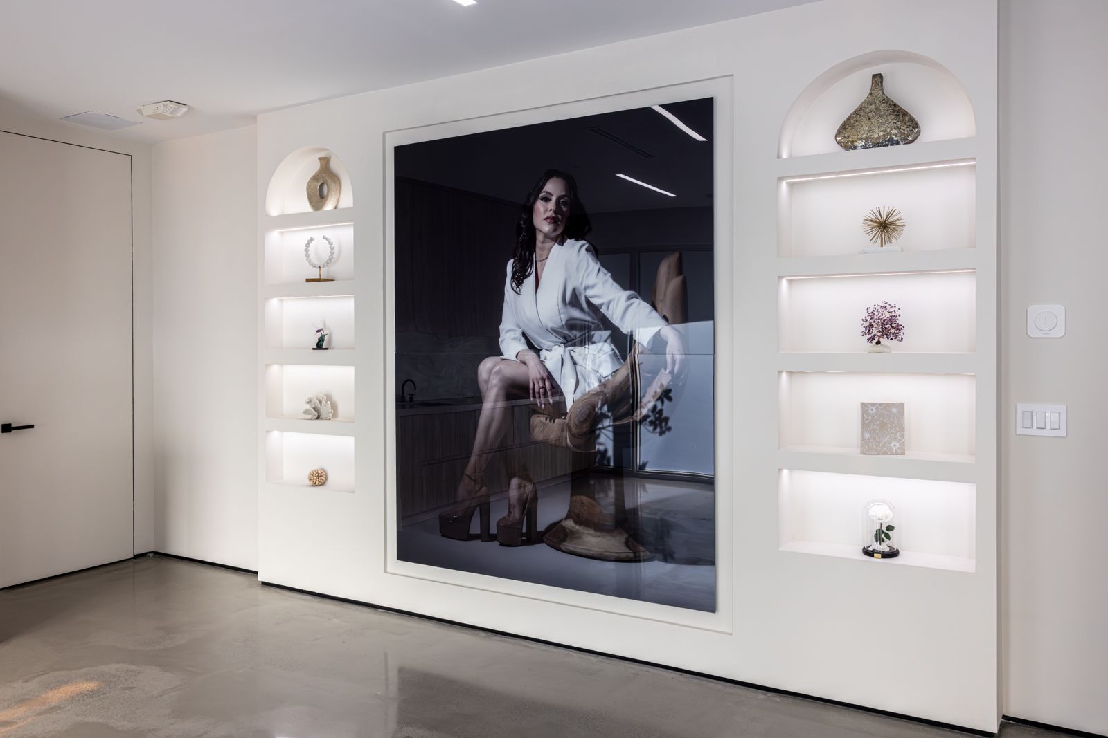 A large portrait of a seated person centered on a white wall flanked by symmetrical, illuminated arched wall niches.