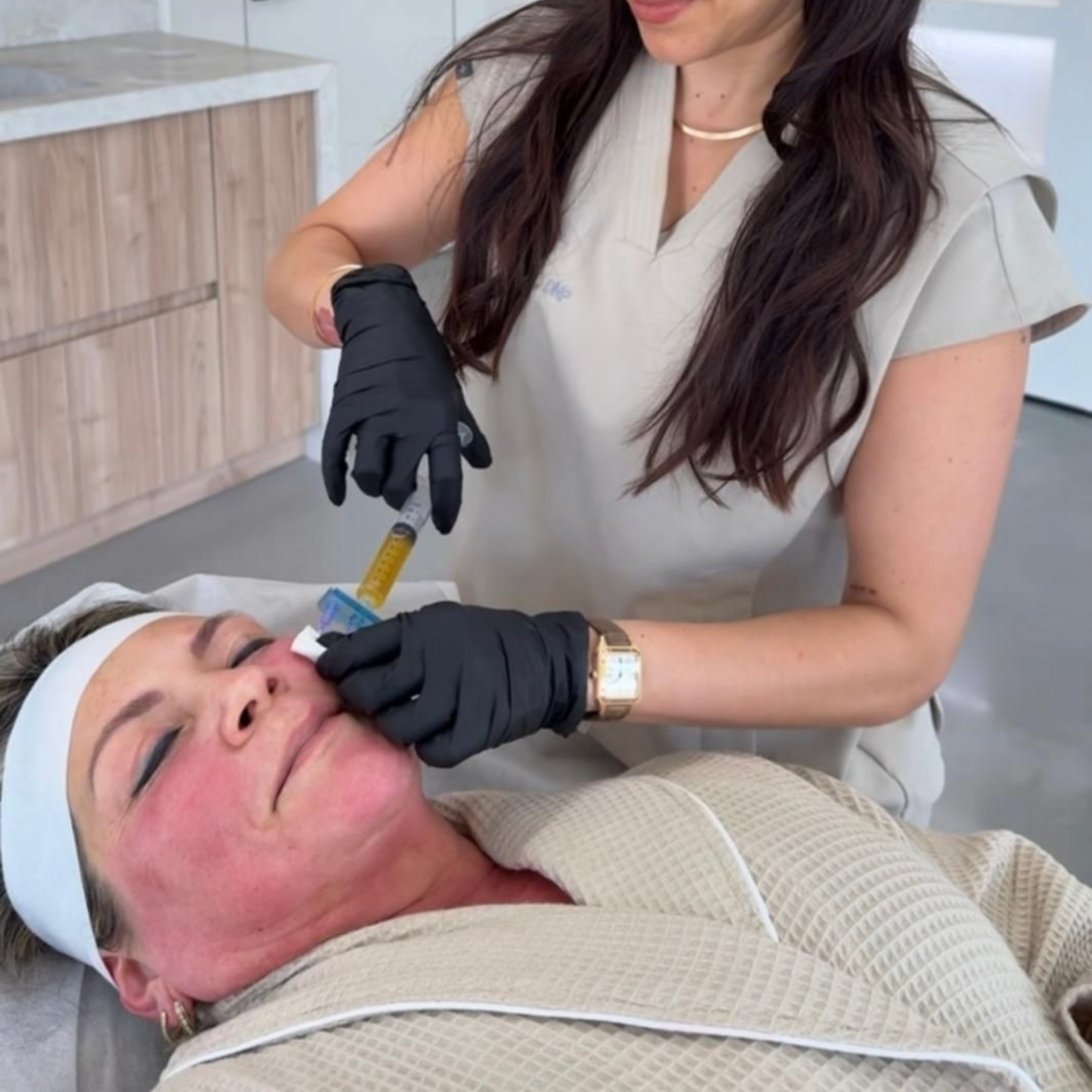 A practitioner in black gloves administers a yellow liquid via syringe into a patientโs cheek during a medical procedure.