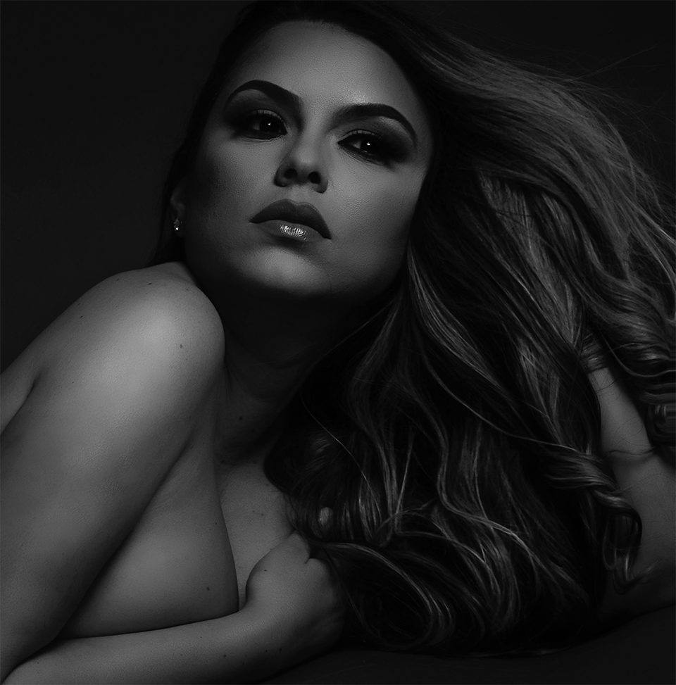 A black and white portrait of a person with long, flowing hair, posing with a focused expression in soft, dramatic lighting.