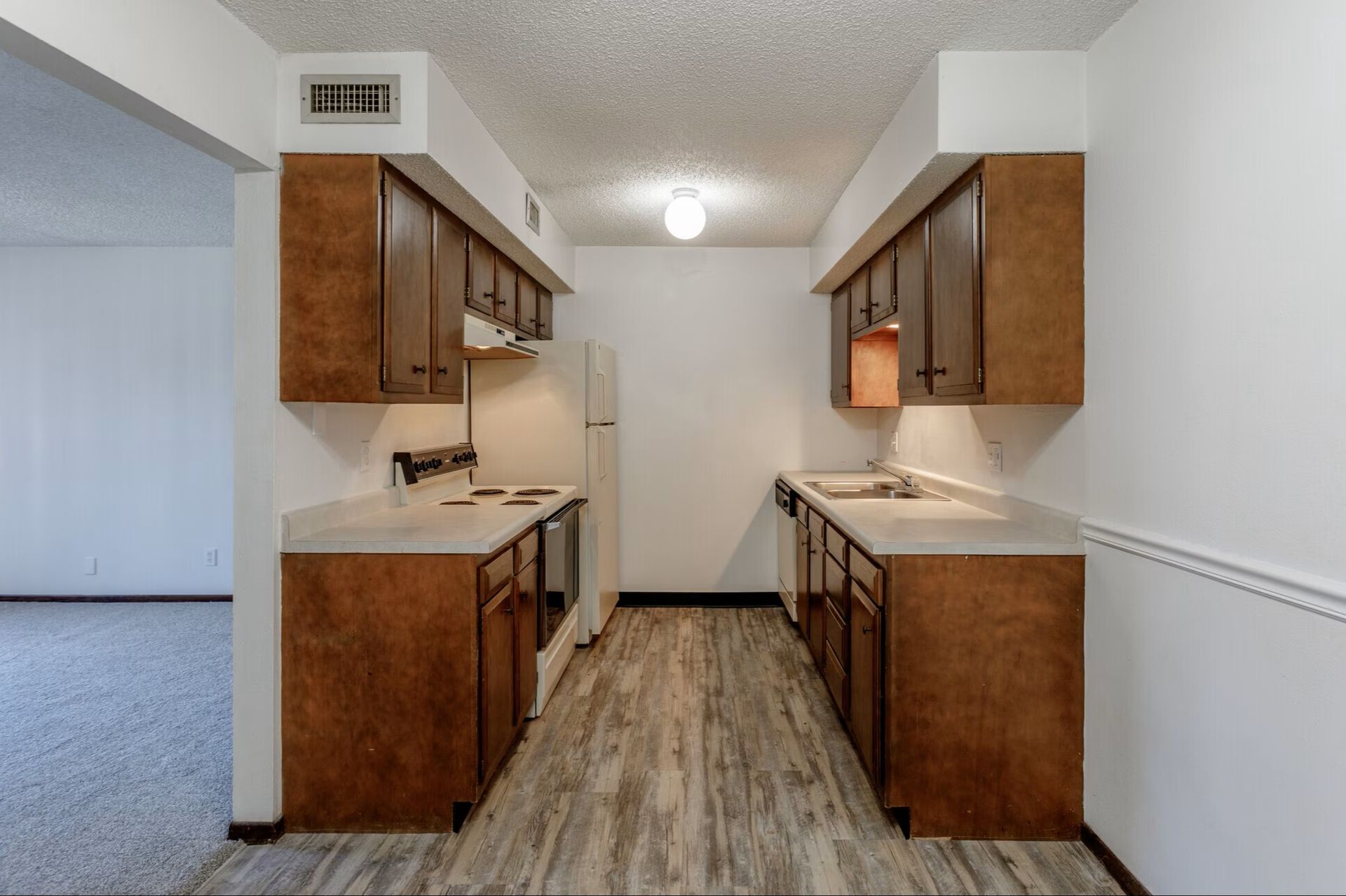 Empty living room with beige carpet, ceiling fan, and small kitchen pass-through.