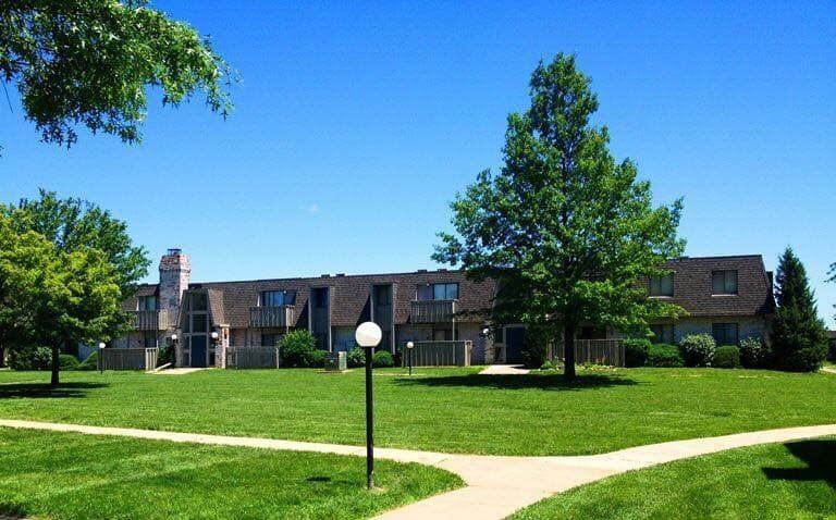 Apartment building with green lawn, trees, and walking paths on a sunny day