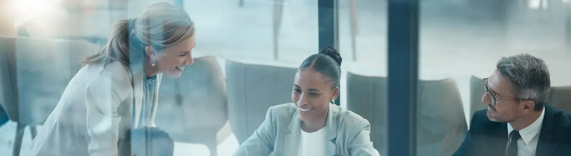Three businesspeople in a meeting, discussing at a conference table in a modern office.