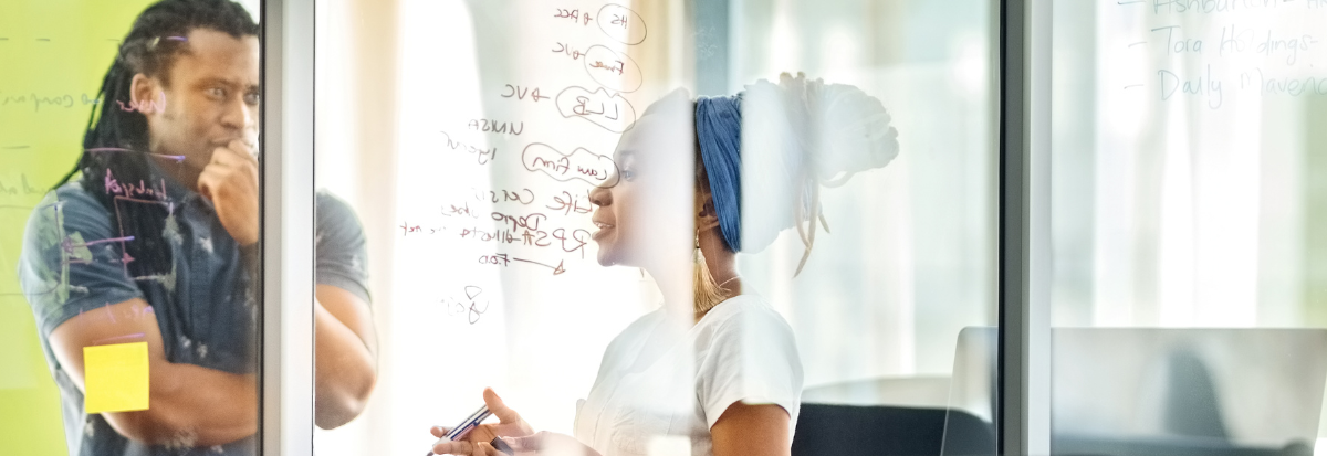 Two people discussing a project, brainstorming on a glass wall in an office setting.