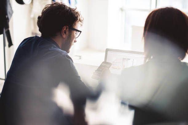 Man and woman looking at a laptop screen in a bright office. The man points, discussing a design.