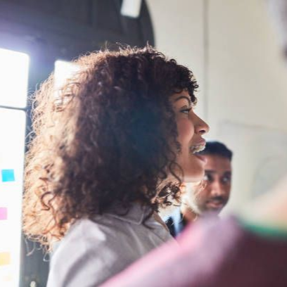 Woman speaking in a bright meeting room, with a man in the background