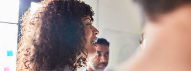 A woman with curly hair speaking in a meeting, with another person visible in the background.