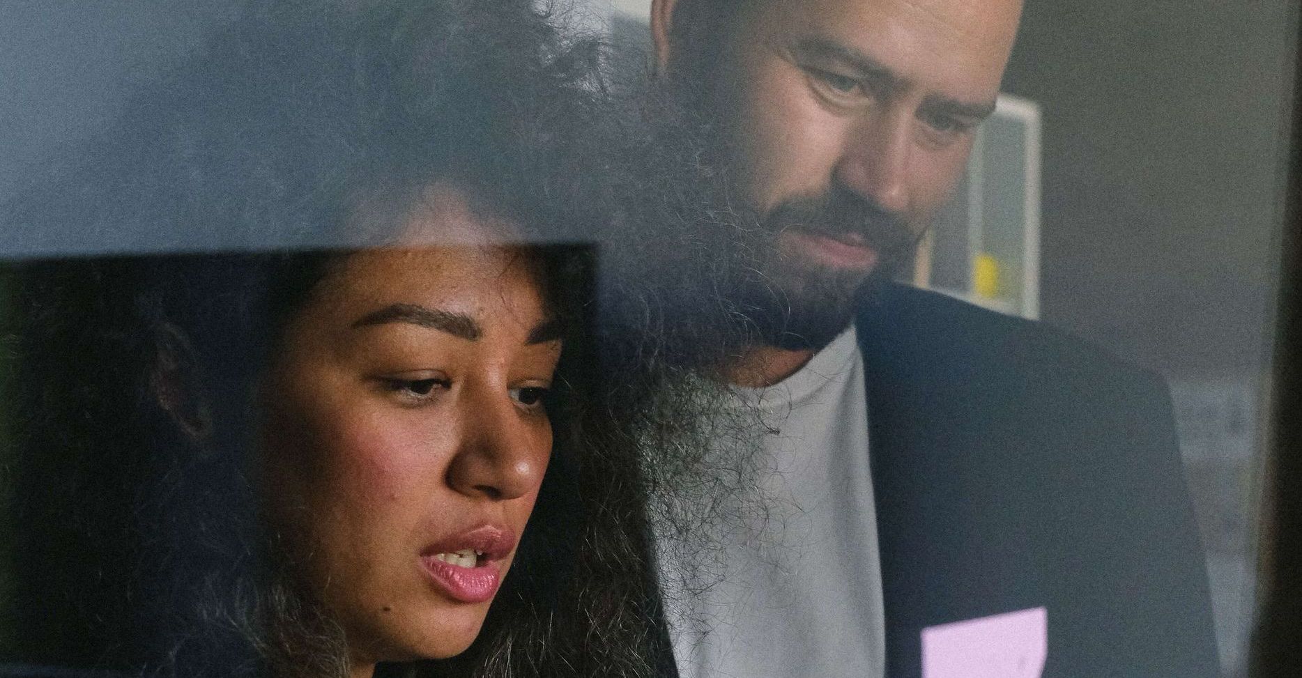 Woman and man looking at something, likely a document, with concerned expressions. Office setting.