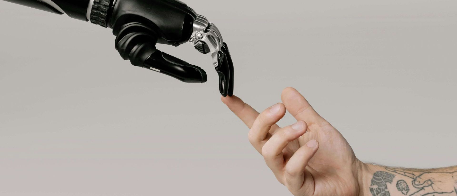 A prosthetic hand touching a human finger. One is black and metallic, the other is flesh-toned with tattoos.