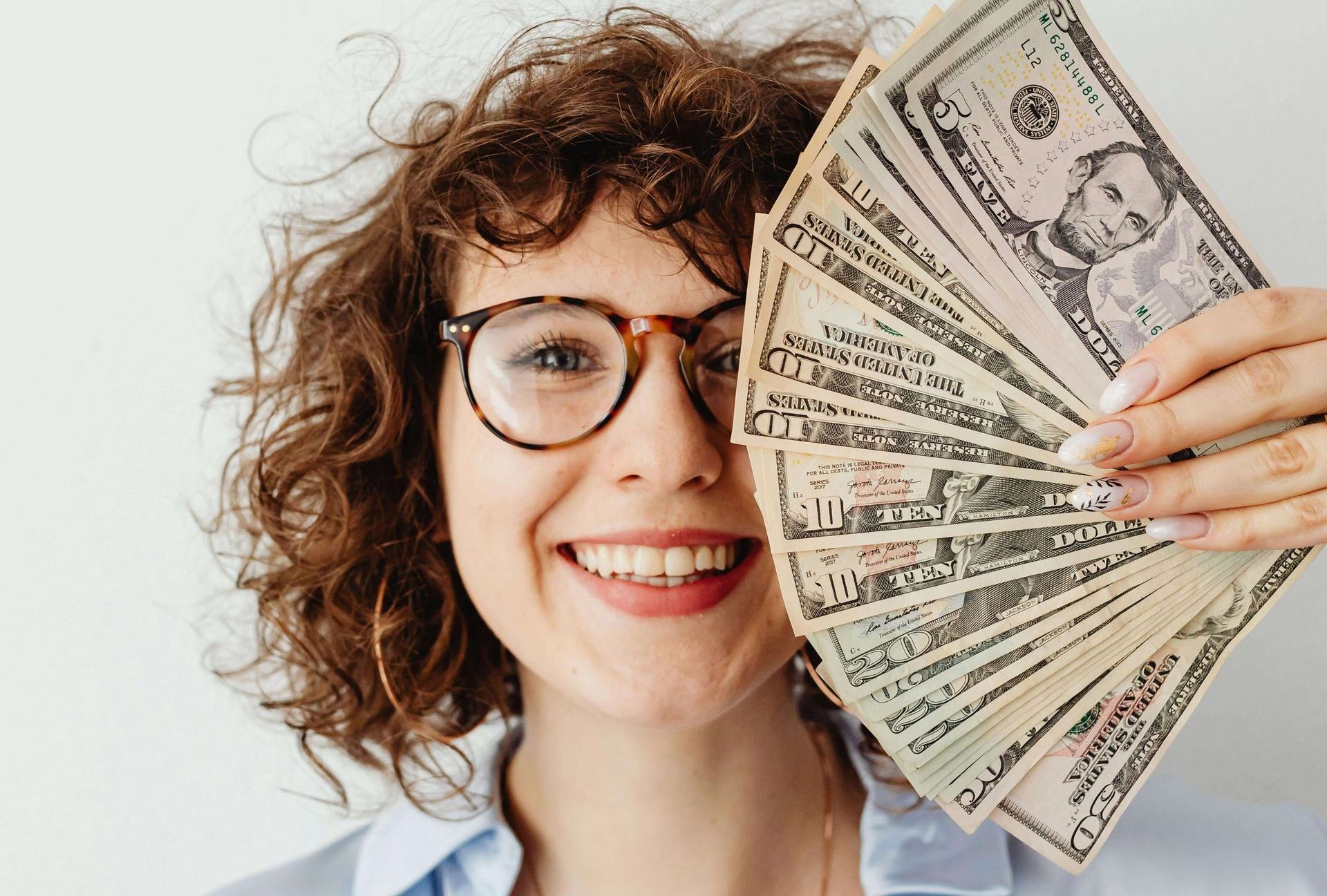 Woman with glasses smiling, fanning out US dollar bills.