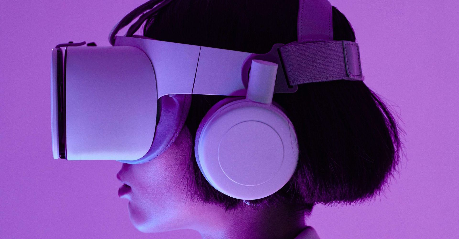 Person wearing a white VR headset and headphones, lit with purple light.