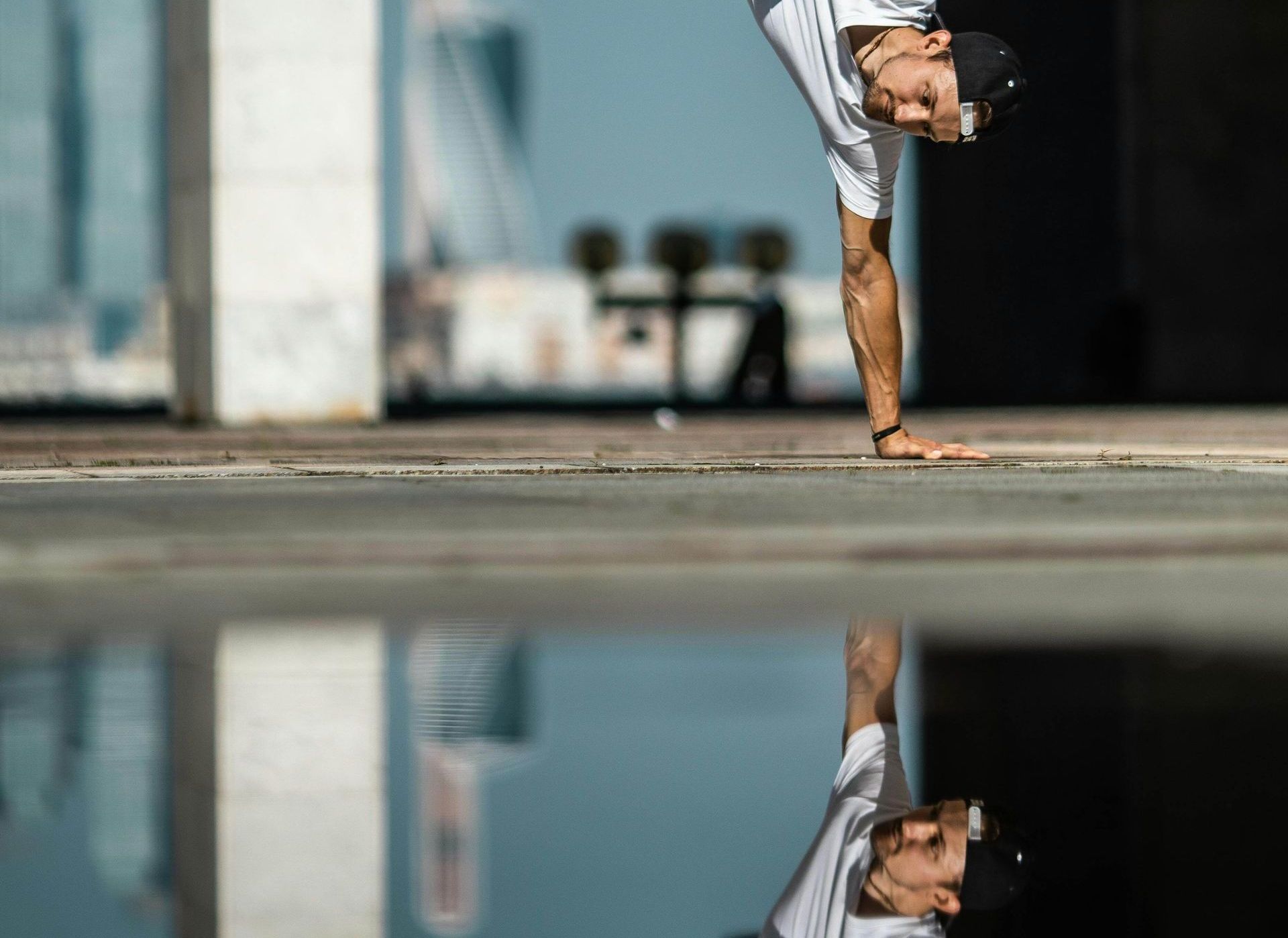 Man doing a handstand reflected in a puddle. Urban setting, sunny day.
