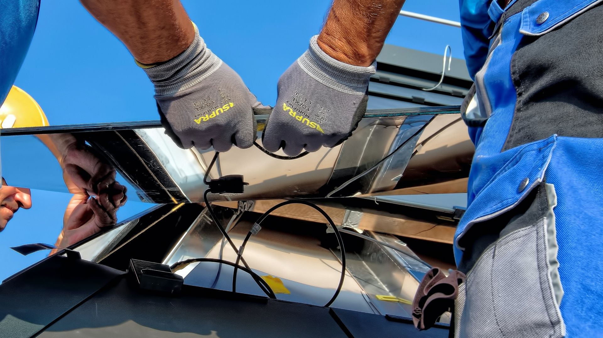 Hands wearing gloves connecting wires on solar panels.