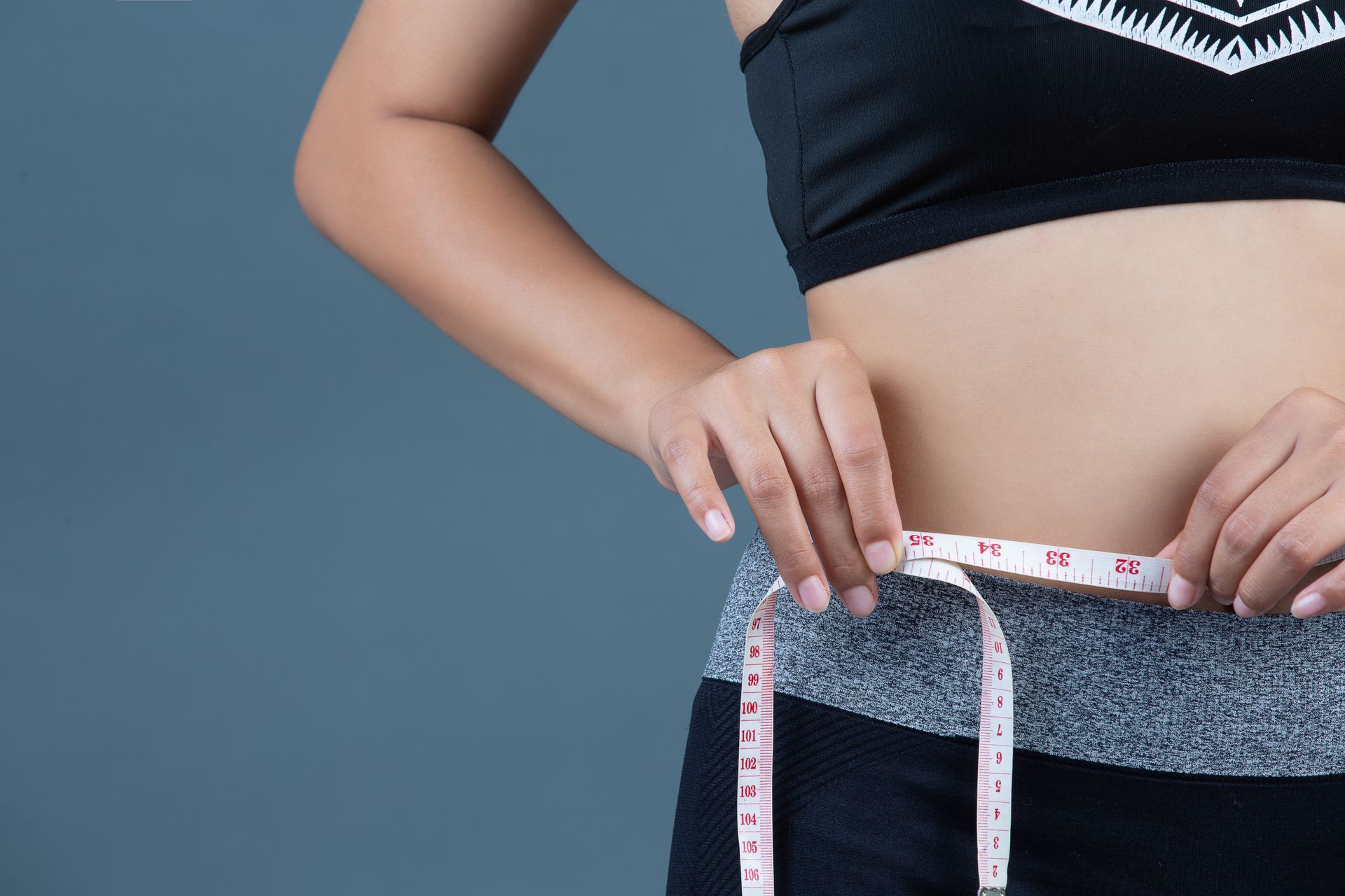 Hands measuring waist with a tape measure against a blue background.