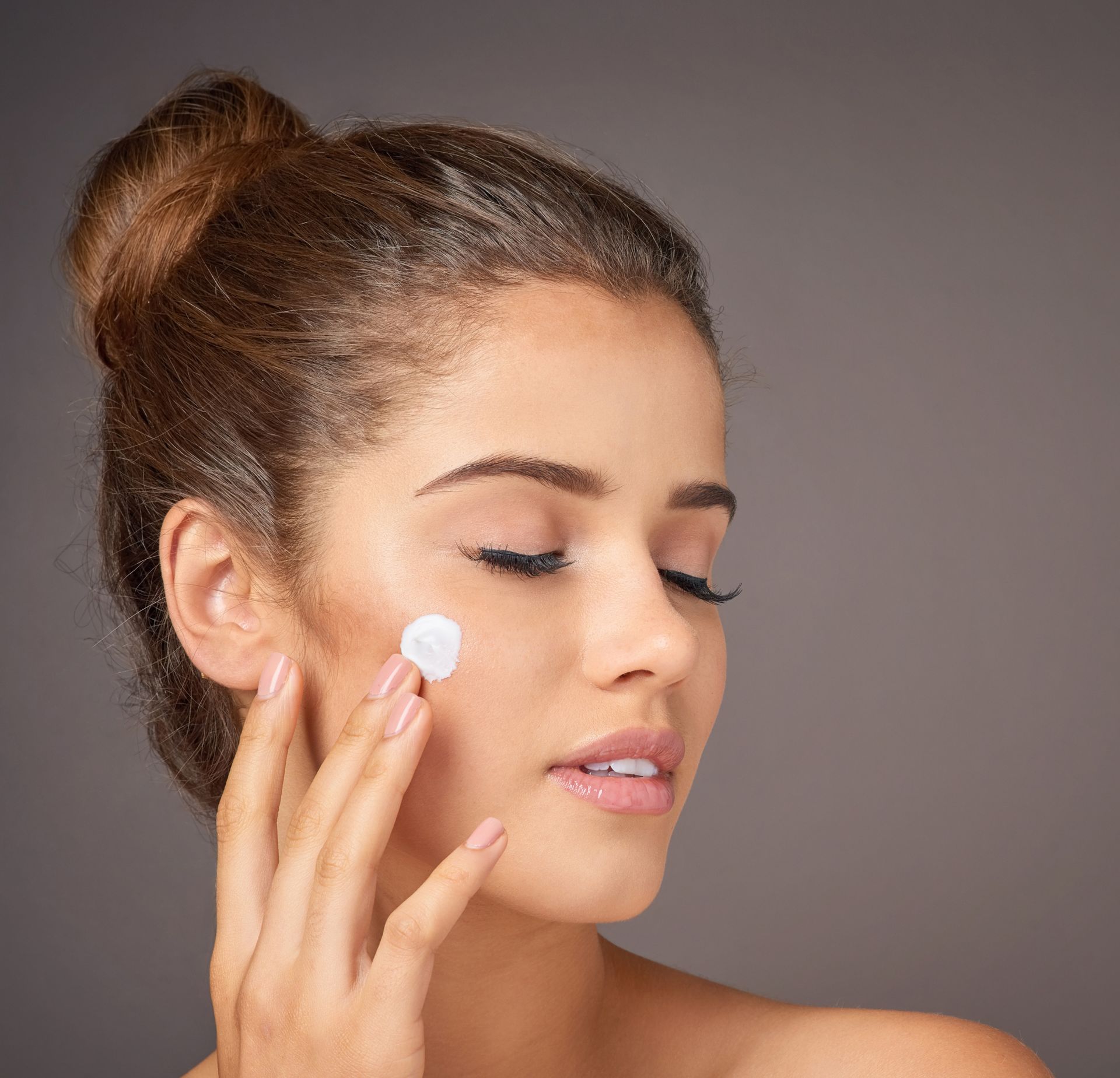 Woman applying white cream to her cheek against a gray background