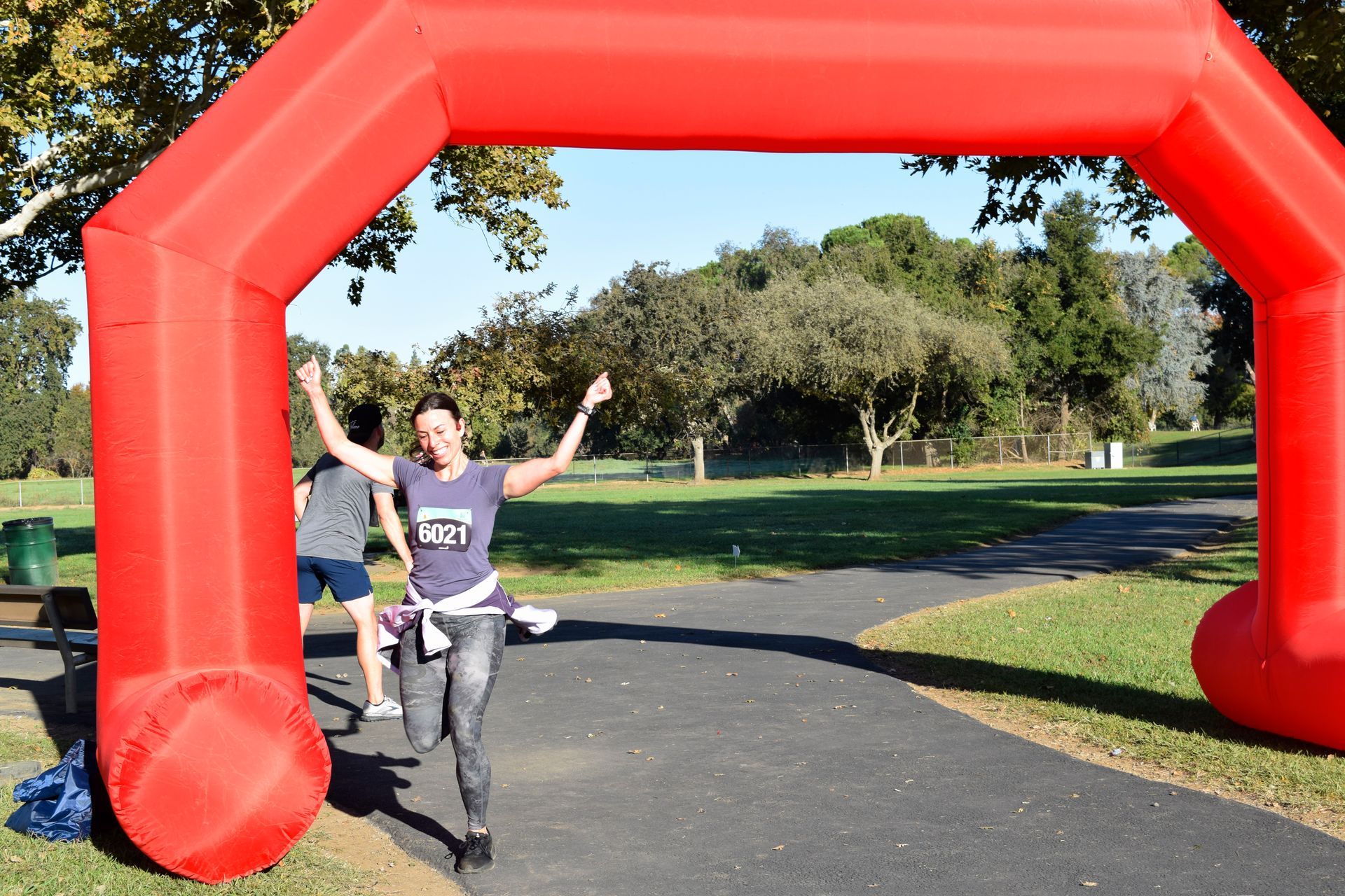 Woman celebrates under red inflatable arch after run in park.