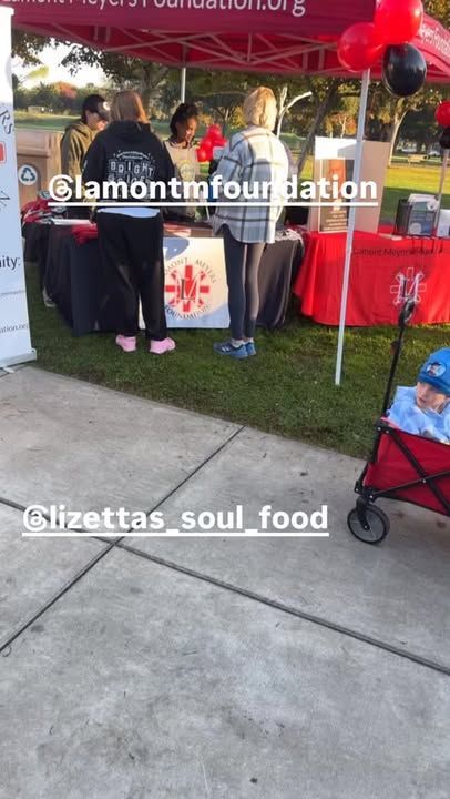 People at a booth with red and black balloons; grass and concrete in foreground.