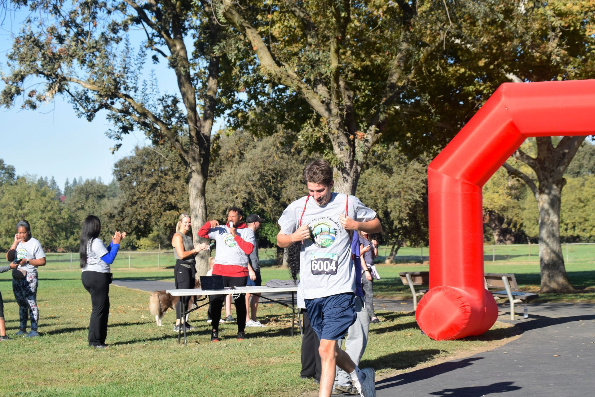 Runner crossing finish line at an outdoor race, red arch, cheering people in background.