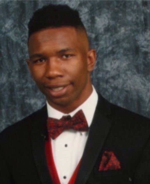 Man in a tuxedo with a burgundy bow tie and pocket square, smiling.