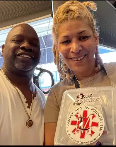 Two people smiling, holding a container with a foundation logo.