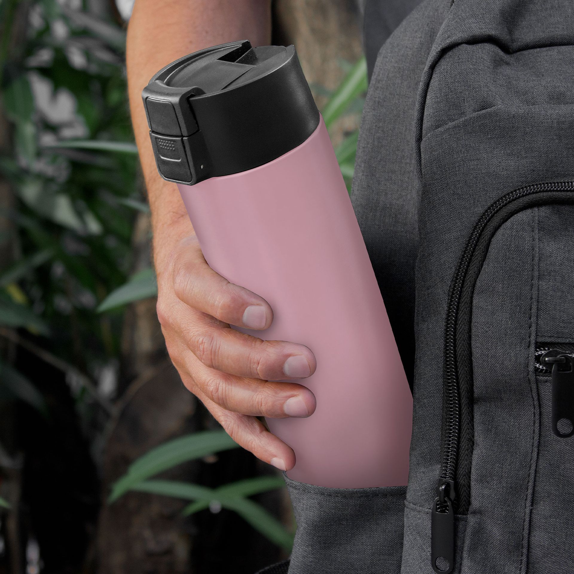 Hand holding a pink insulated water bottle beside a gray backpack outdoors