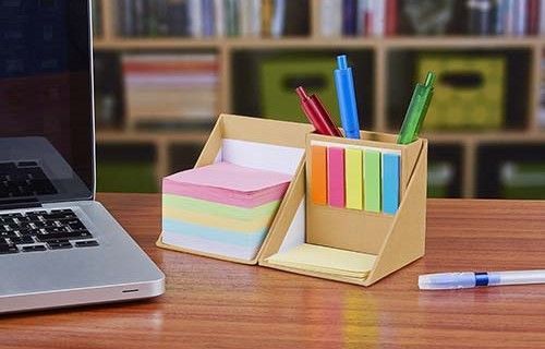 Desk with laptop and colorful sticky notes in two pen holders, with pens on a wooden table