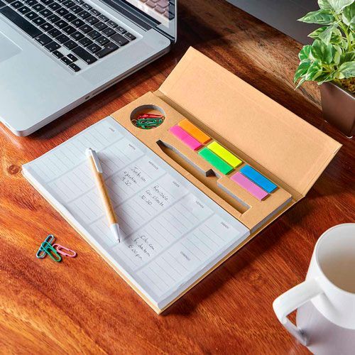 Desk with planner, pencil, sticky notes, laptop, coffee mug, and plant on a wooden table.