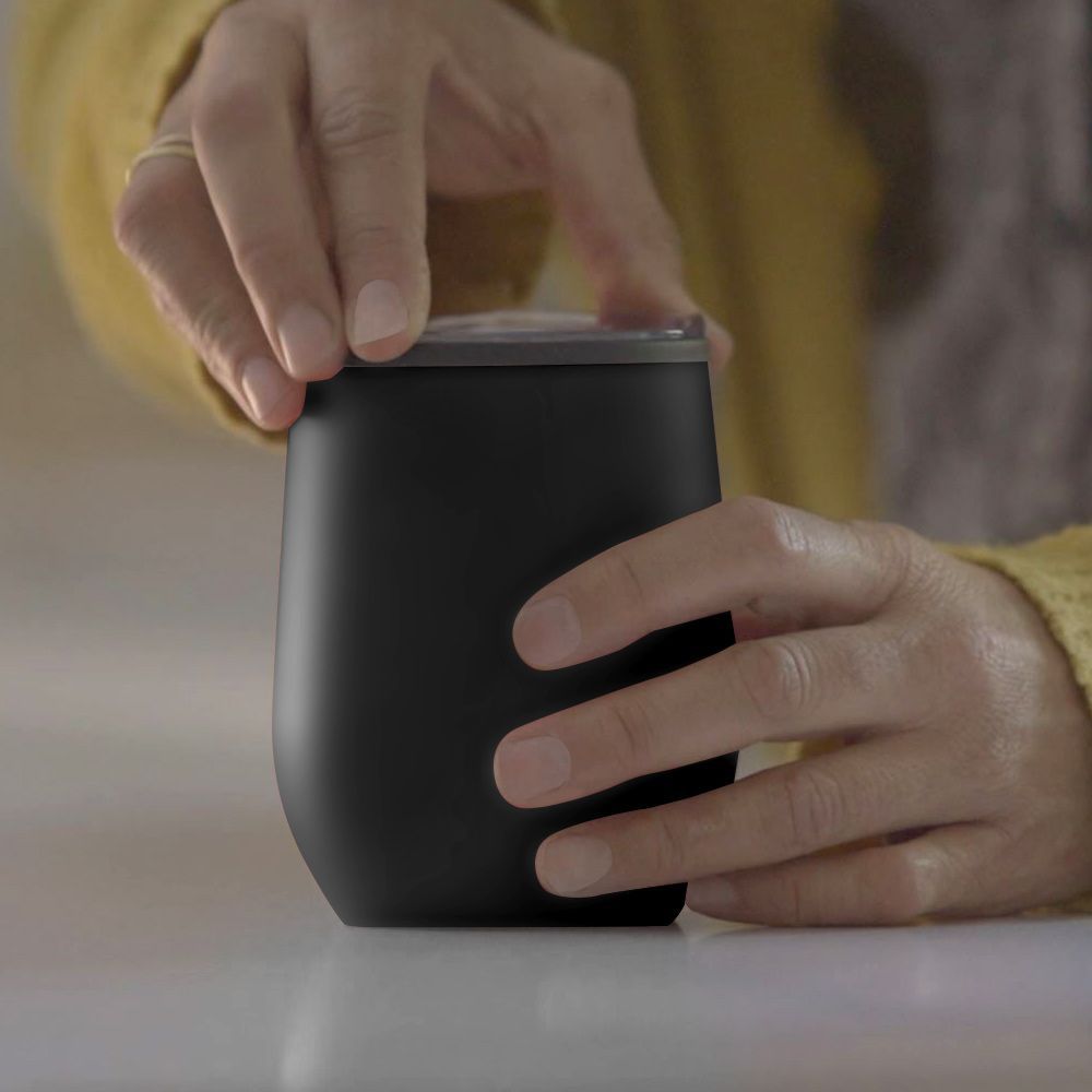 Hands holding a small black cup while lifting its silver lid on a table