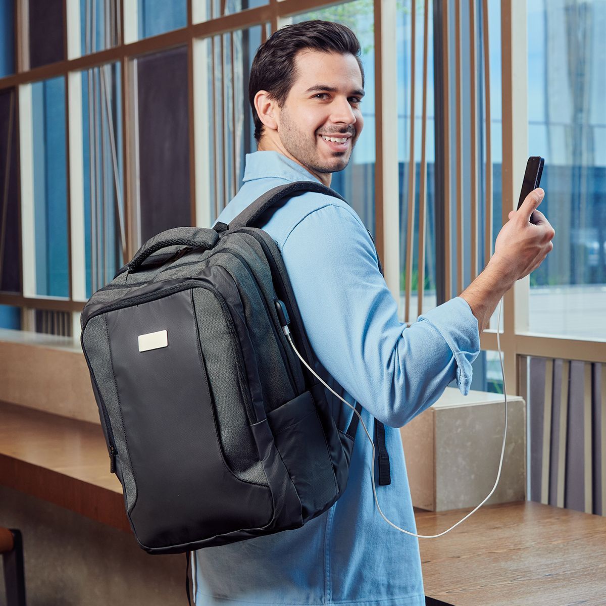 Smiling traveler with backpack holding a phone in a modern building hallway