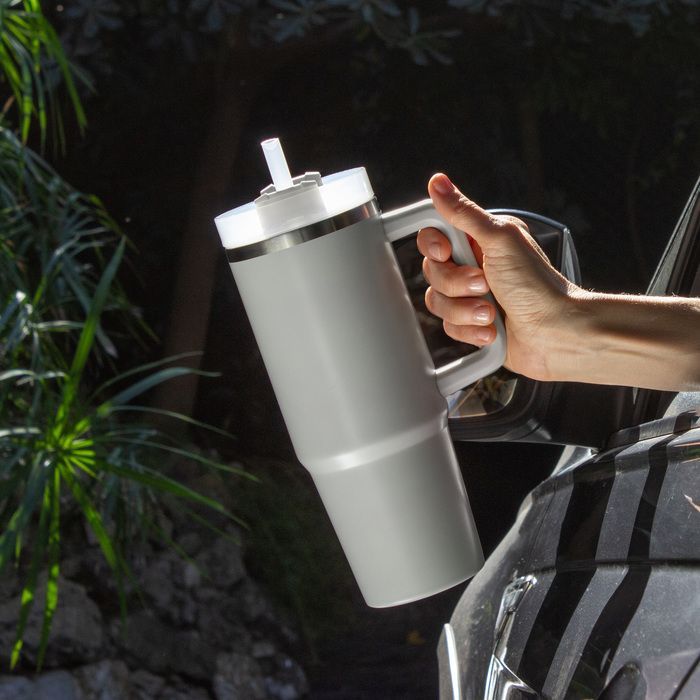 Hand holding a gray insulated tumbler with a clear lid outdoors in sunlight