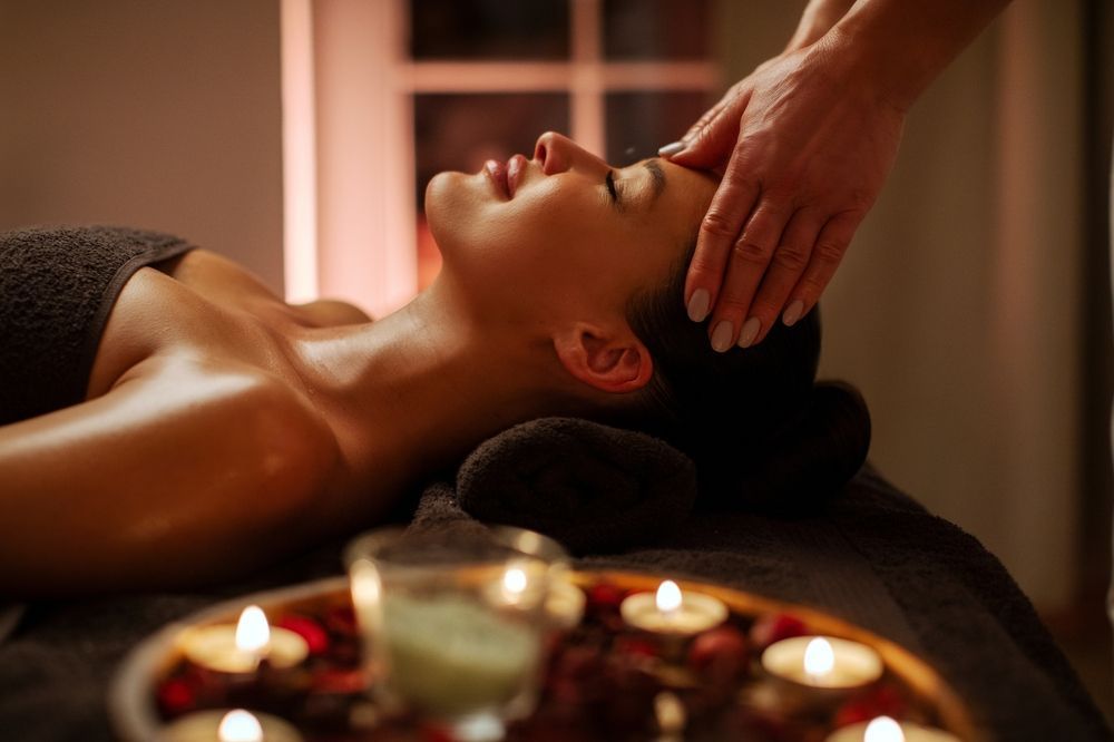 Spa massage with woman reclining and therapist’s hand on her forehead, candles in foreground