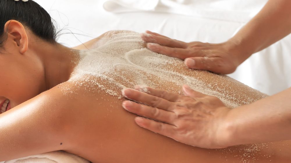 Person receiving a back massage with exfoliating cream on a white bed