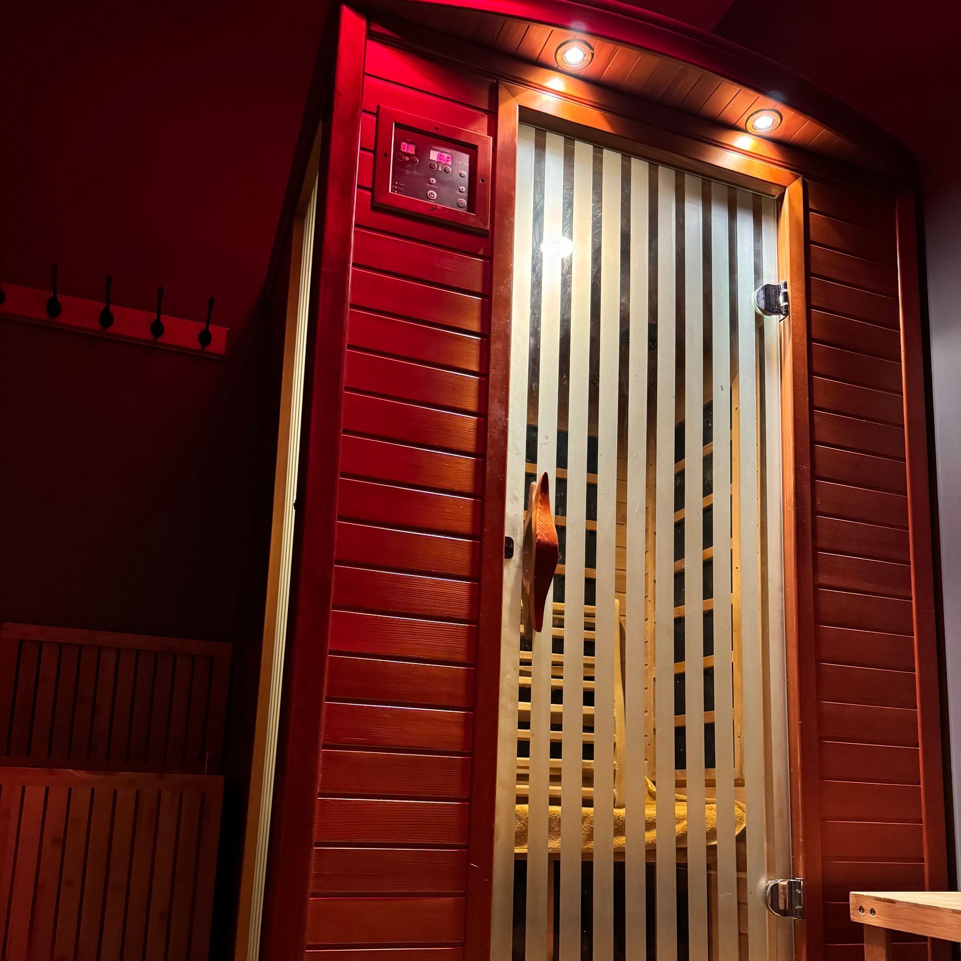 A wooden sauna with a glass door and a red ceiling.