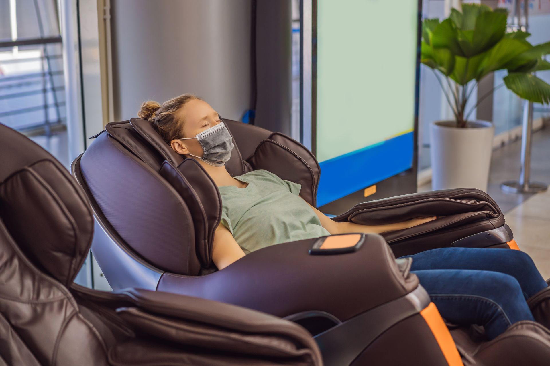 A woman wearing a mask is sitting in a massage chair.