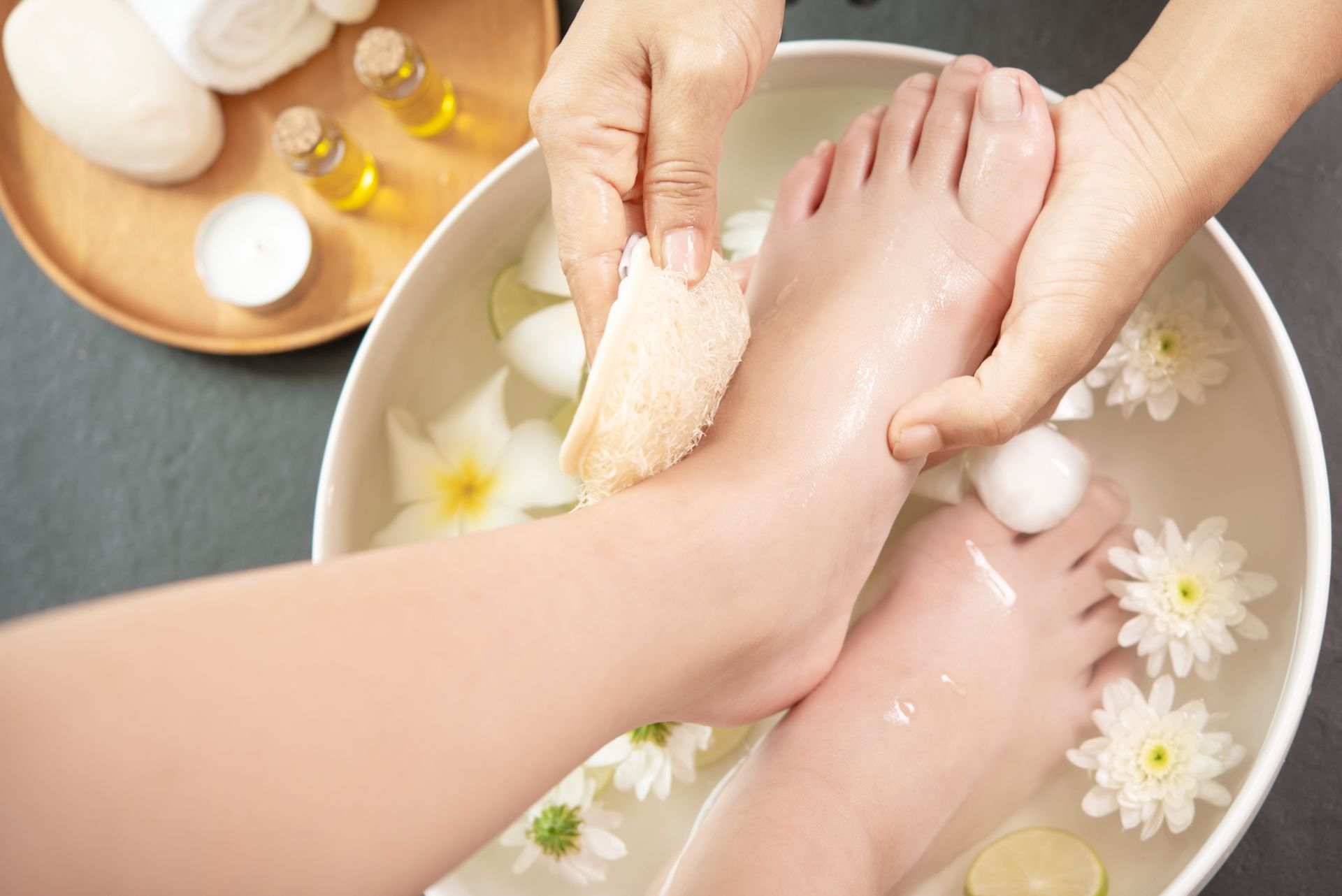 A woman is getting a foot massage in a bowl of water with flowers.