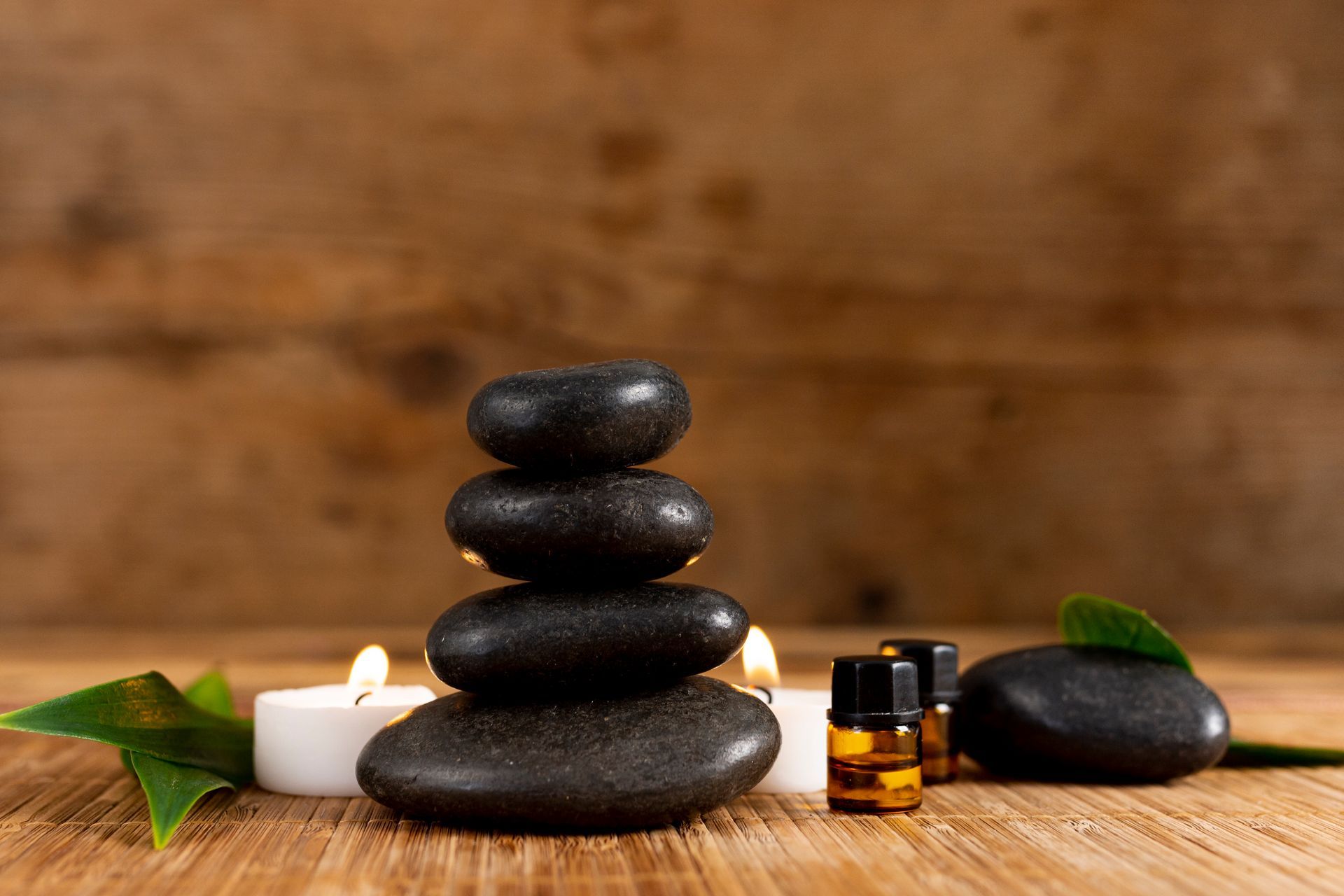 A stack of black rocks with candles and essential oils on a wooden table.