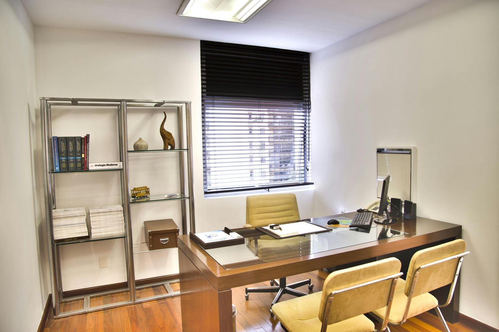 Büro mit Schreibtisch, Stühlen, Regalen und Fenster mit Jalousien; Hartholzboden.