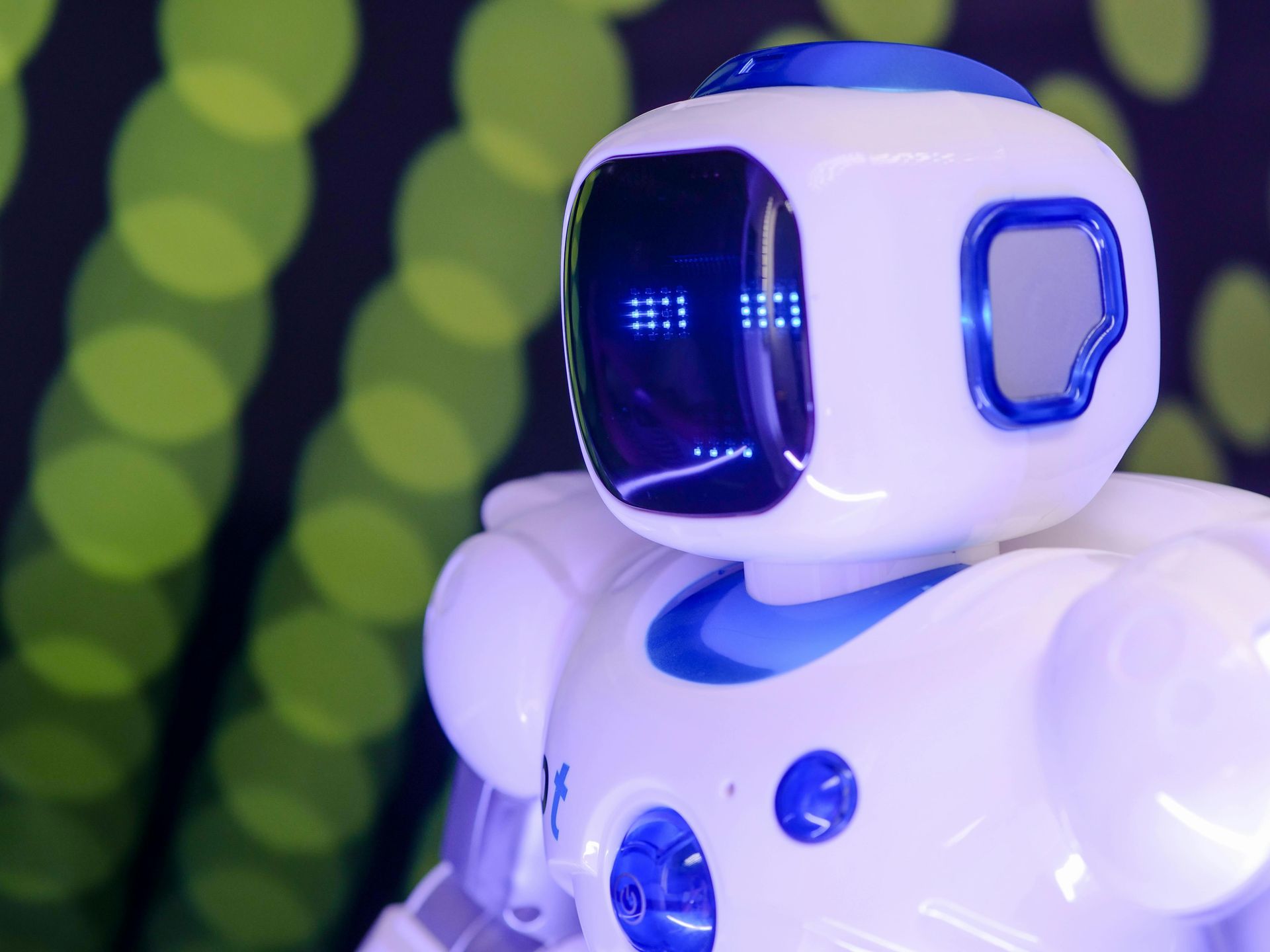 Weiß-blauer Roboter mit einer digitalen Anzeigefläche, der vor einem grünen Bokeh-Hintergrund zur Seite blickt.