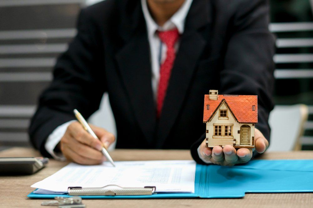 Man Signing A Contract While Holding Miniature House — Okmulgee, OK — Greg Marriott CPA PLLC