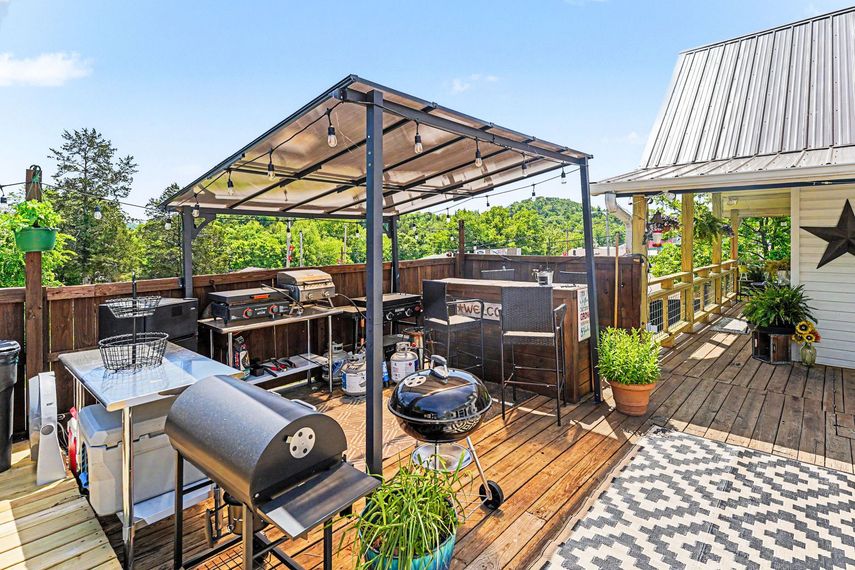 Backyard patio with metal gazebo, grill, wood deck, and potted plants beside a house
