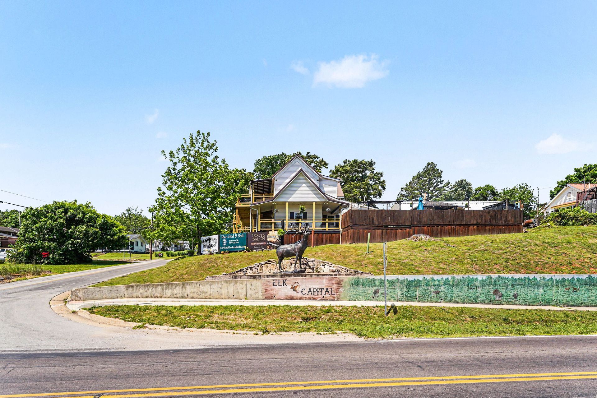 Residential house on a corner lot with a curved driveway, trees, and a bright blue sky