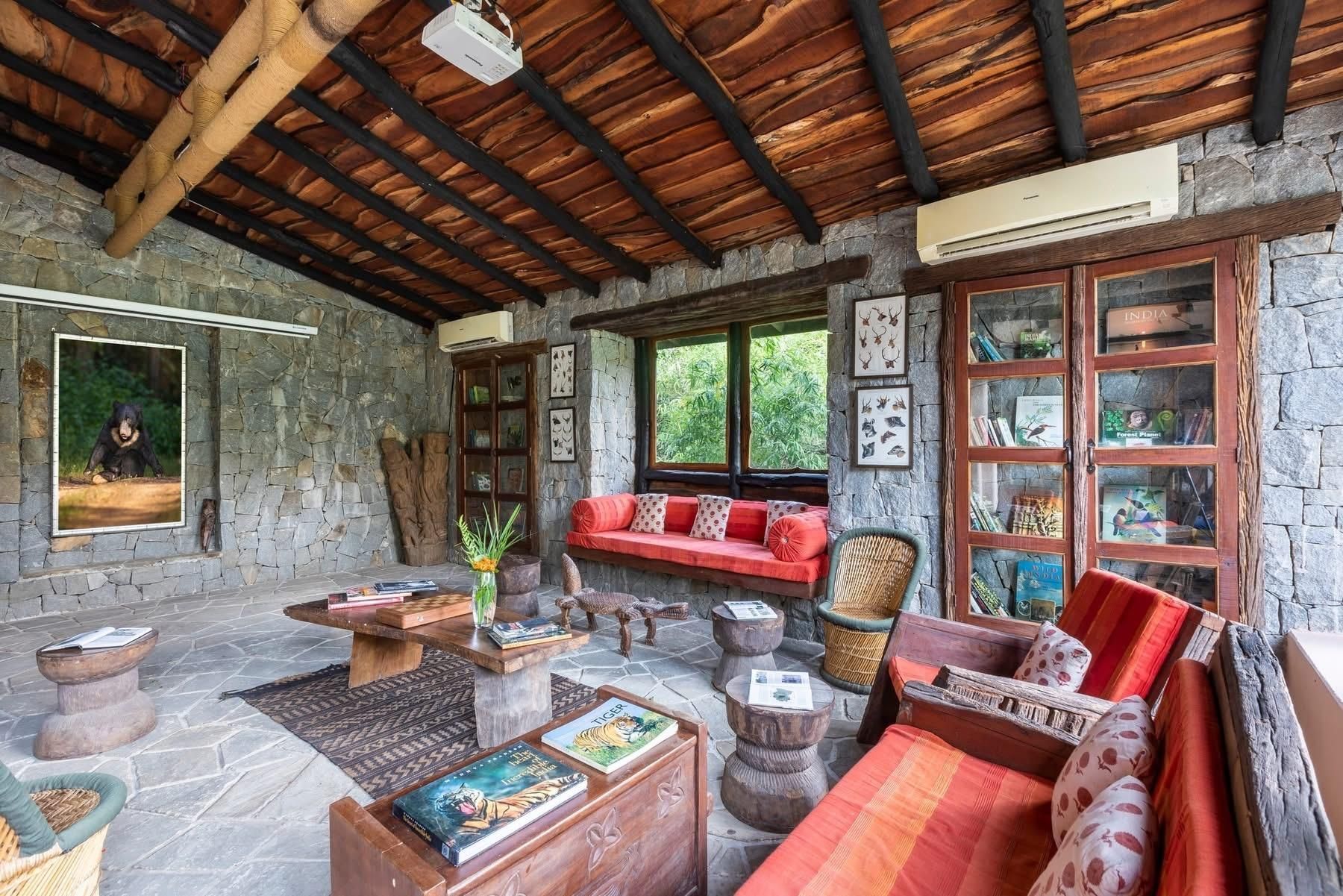 Cozy rustic living room with red sofas, wood beams, stone walls, and large windows