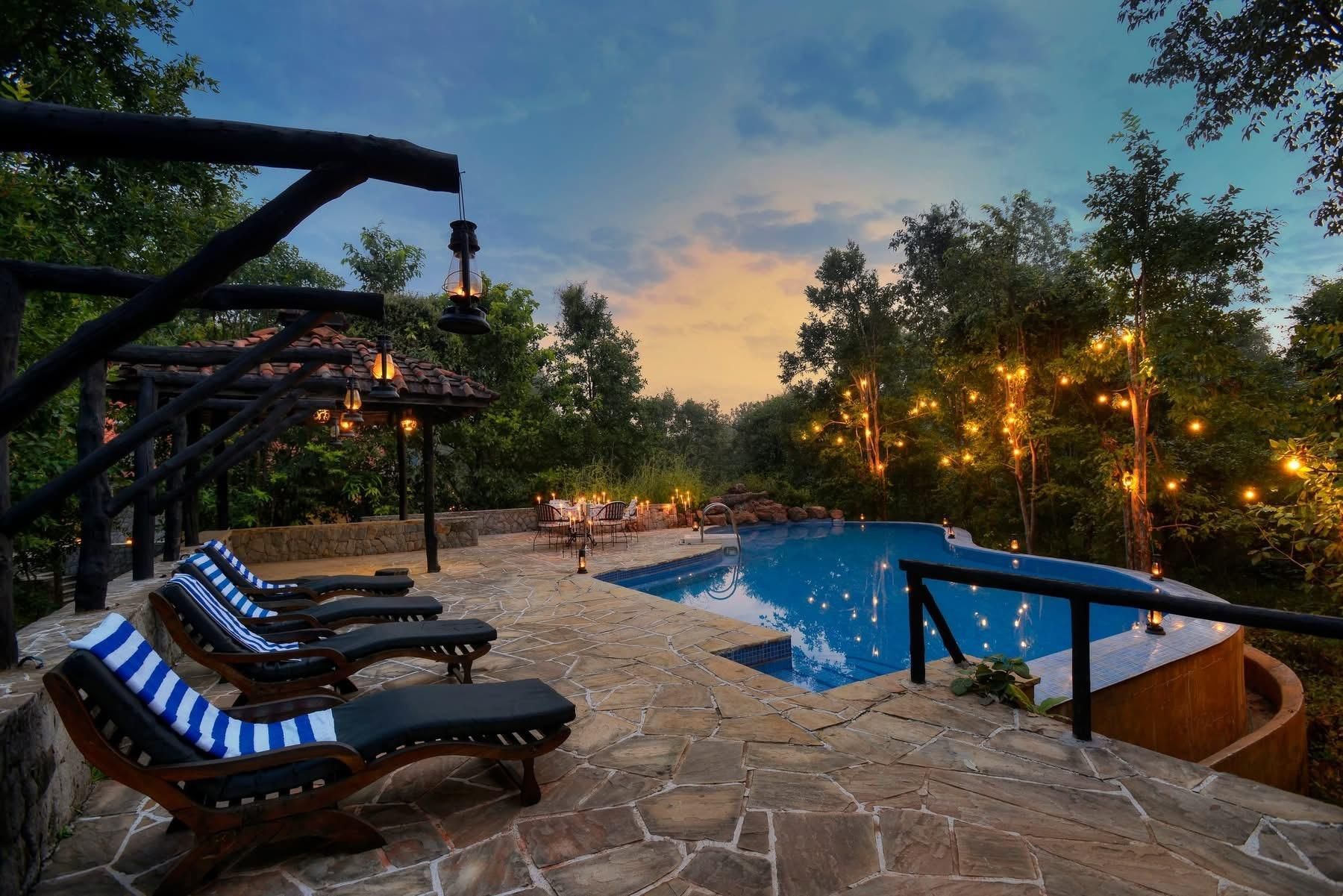 Stone patio with lounge chairs overlooking a lit backyard pool at dusk