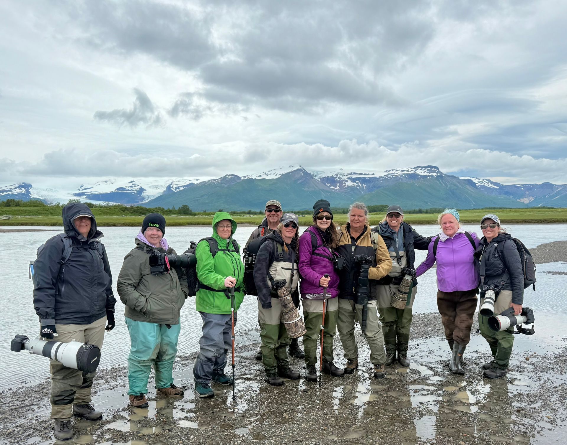 Group of people in outdoor gear standing in a muddy marsh with snowy mountains in the background.