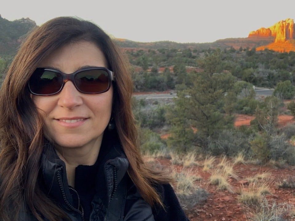 Woman wearing sunglasses in a desert landscape with rocky hills at sunset