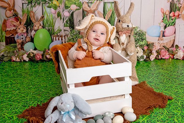 A baby in a bunny costume is sitting in a wooden crate.