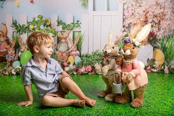 A little boy is sitting on the grass next to stuffed easter bunnies.