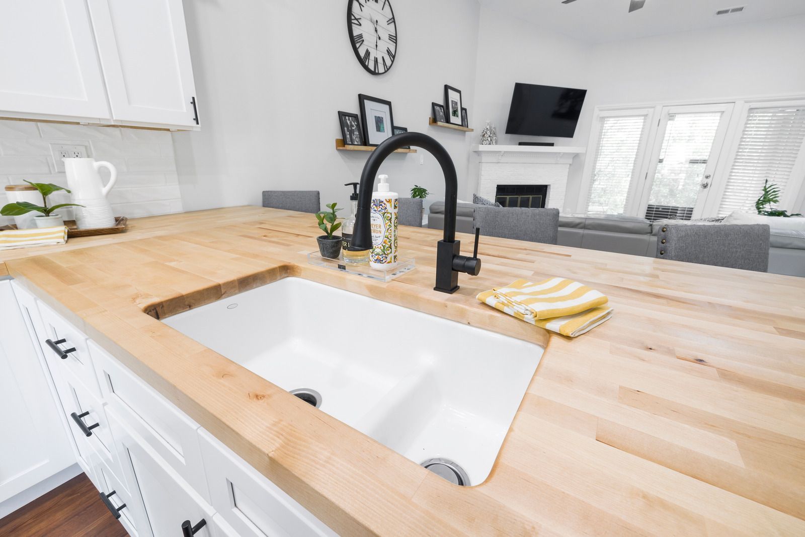 Bright kitchen with farmhouse sink, butcher-block island, and black faucet overlooking a living room.