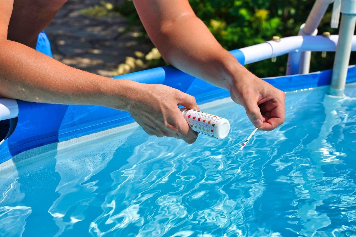 Hands testing pool water with a thermometer beside blue pool water
